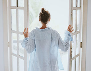 Frau steht an einer geöffneten Fenstertüre als Symbol für frische Haut